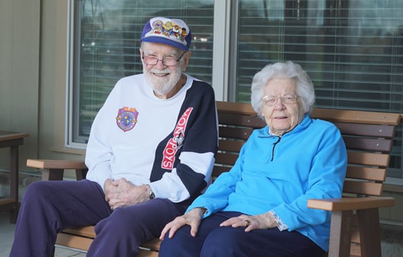 senior man and woman sitting on porch bench