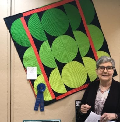 Woman standing in front of a green spiral quilt displayed at a show.