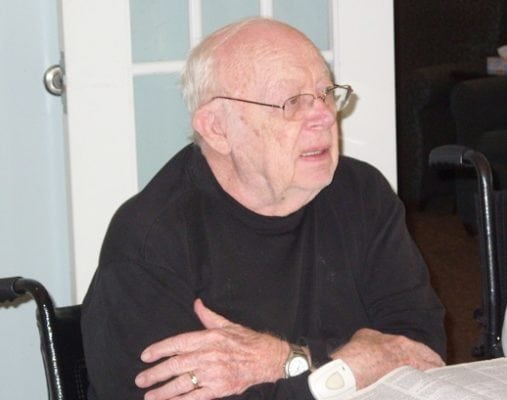 Older man wearing glasses and black sweater sitting at table
